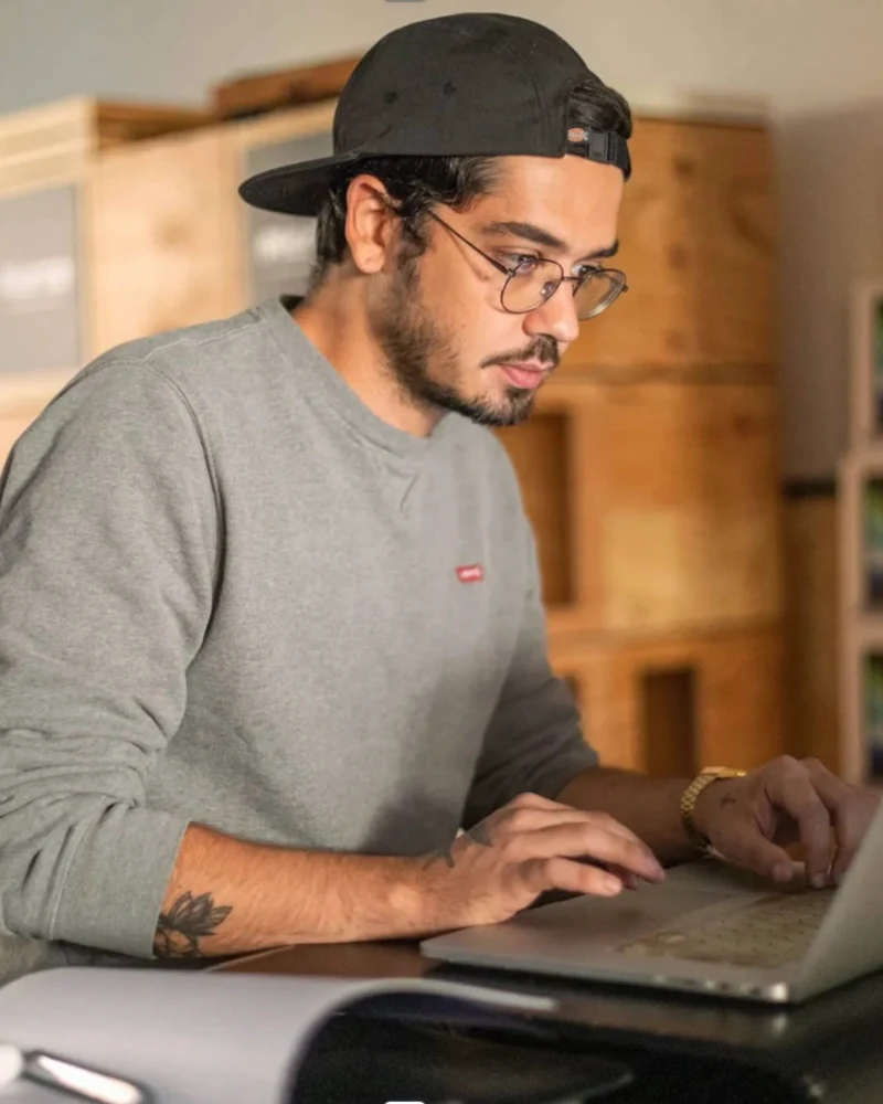 Portrait de Ben, casquette et lunettes, au travail sur son ordinateur portable